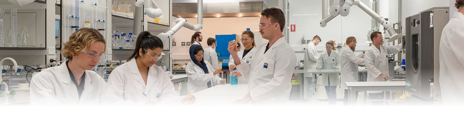 Researchers in lab coats and safety glasses working at benches in the QUT research laboratory